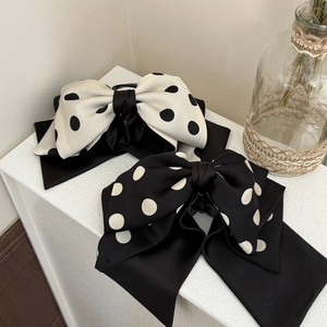 Detailed close-up of large polka dot bow hair clips in elegant black and white silk fabric