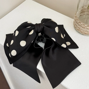 Detail of a large black satin bow hair claw clip with white polka dots on a clean white desk