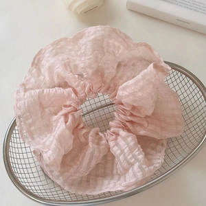 Détail d'un chouchou en seersucker rose clair à carreaux placé dans un panier métallique