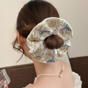 Détail d'un chouchou en satin beige brodé avec oiseaux et feuilles dorées sur chignon
