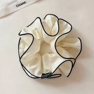 Dettaglio scrunchie in seta bianca con bordo nero e etichetta in tessuto cucita