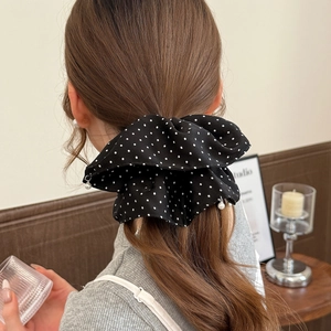 Black polka dot scrunchie with pearl pendant detail on a woman's hair in a home setting