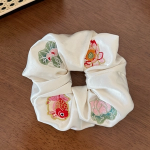Détail de carpes koï et lotus brodés sur un chouchou en soie crème de style chinois
