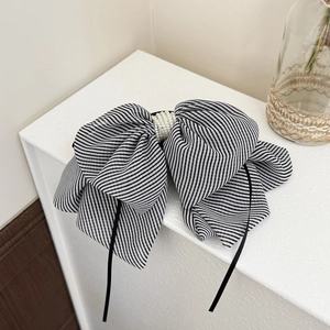 Detailed view of large black and white striped bow hair clip with faux pearl center and ribbons