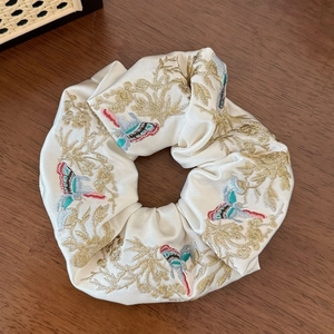 Détail d'un chouchou en soie crème avec des broderies dorées de plantes et de papillons
