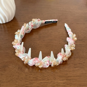 Close-up of floral fabric headband with crystals and white cone studs on wooden background
