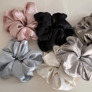 Close-up of six glossy satin scrunchies in assorted colors with soft silk texture