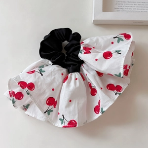 Detail of white ruffled scrunchie with red cherry prints on a beige surface