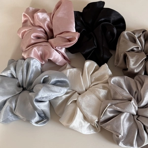Detail shot of assorted glossy satin scrunchies in pink, black, and neutral tones