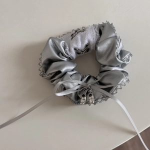 Close-up of silver satin hair scrunchie with lace edge and ballet slipper metal pendant