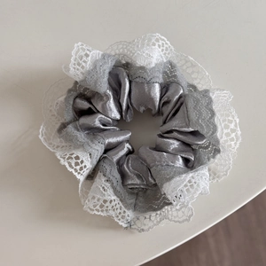 Close-up of silver satin scrunchie with delicate white lace trim and elegant textures