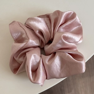 Detailed view of large pink satin scrunchie showing glossy texture and rich pleated design