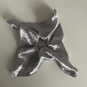 Macro view of silver metallic satin scrunchie showing glossy texture and star-shaped folds