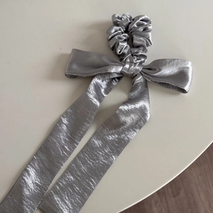 Detailed view of silver satin bow scrunchie with lace edges and long flowing ribbons