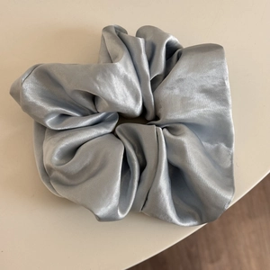 Close-up of glossy silver-grey satin scrunchie with elegant silk-like pleated texture