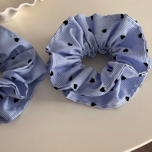 Gros plan de deux chouchous à rayures bleues et motifs de cœurs noirs sur tissu doux