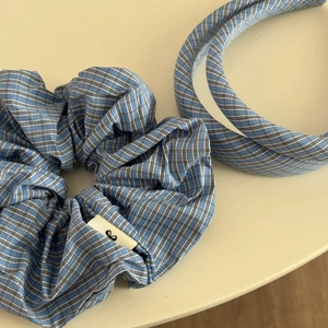 Détail de l'ensemble chouchou à carreaux bleus avec logo tissé sur fond minimaliste