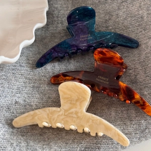 Three acetate hair claws in dark blue, tortoise, and cream marble on grey knit fabric