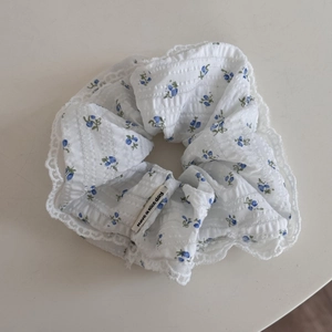 Close-up of white floral scrunchie with blue pattern, lace edge and decorative label