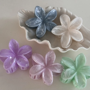 Detail view of five marble texture plumeria hair claws on a white shell tray