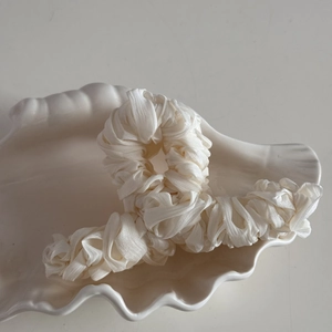 Close-up of pleated cream silk fabric texture on a large hair claw clip in a shell dish