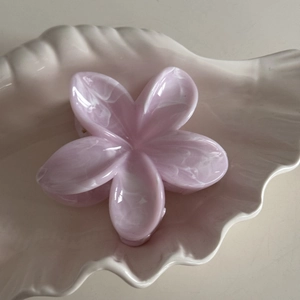 Macro detail of a pink marble-textured frangipani hair claw clip on a shell tray