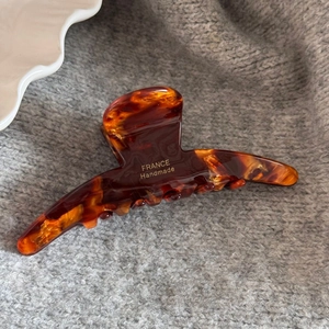 Detailed view of large tortoiseshell hair claw with gold France Handmade logo on grey fabric