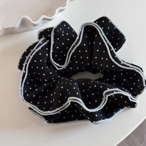 Detail of black polka dot scrunchie with white piped edges and pleated fabric texture