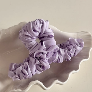 Close-up of lavender pleated fabric hair claw clip on a white shell-shaped tray