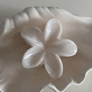 Detail of a creamy white frangipani flower hair claw clip with pearl-like marble finish