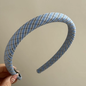 Détail d'un serre-tête en tissu à carreaux bleu ciel et blanc tenu à la main, vue rapprochée