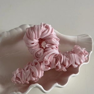 Detailed view of pink silk pleated fabric wrapped shark hair claw on a white shell plate