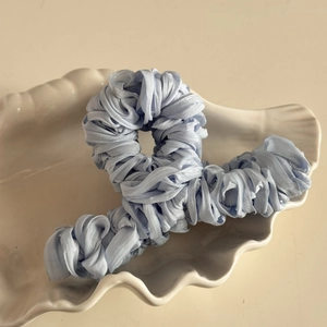 Close-up of light blue pleated silk fabric hair claw clip on white shell ceramic plate