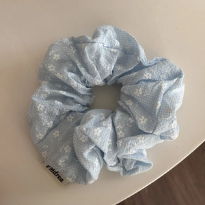 Detalle de un coletero azul claro con flores, cuadros vichy y una etiqueta de marca