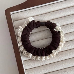 Close-up of coffee brown scrunchie with cream lace edges on a wooden display tray