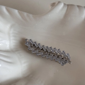 Detailed close-up of leaf-shaped hair clip with square crystals on a ceramic tray