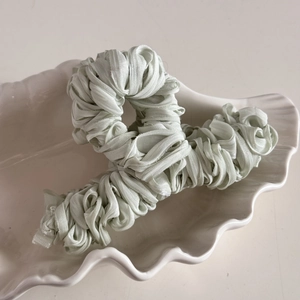Detailed view of sage green mercerized pleated fabric hair claw clip in a shell tray