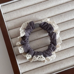 Detailed close-up of dark grey lace scrunchie with white trim and grey bead on velvet tray