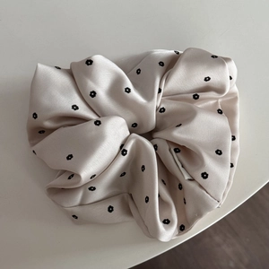 Detailed close-up of a floral satin scrunchie featuring a smooth glossy texture and pleats