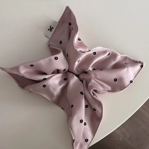 Detailed close-up of pink satin hair scrunchie with black floral print and fabric label