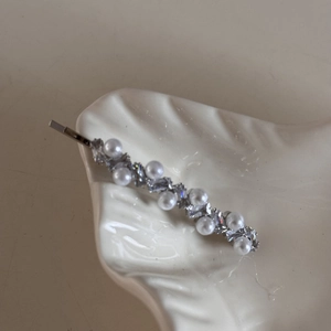 Detail of silver bow hair clip with white pearls and sparkling rhinestones on ceramic tray