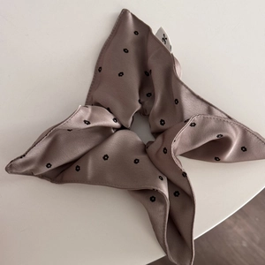 Close-up of satin floral scrunchie with side woven label and dainty bow pattern