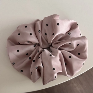 Detail of pink satin scrunchie featuring delicate black floral patterns on silk-like fabric
