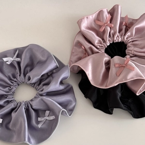 Close-up of three satin scrunchies in purple, pink, and black with small bows