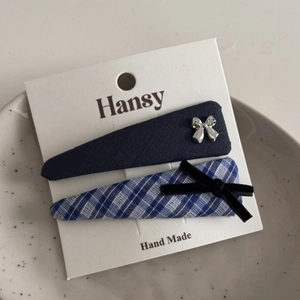 Close-up of blue plaid and navy bow hair clips on a white display card in a ceramic tray