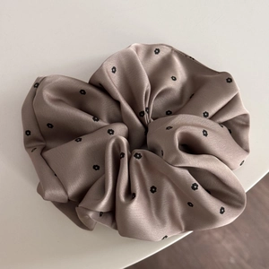 Detail showing smooth satin texture and black floral print on the champagne scrunchie