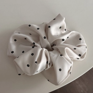 Detailed close-up of smooth satin scrunchie with delicate black floral patterns