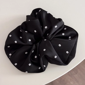 Detailed view of satin floral scrunchie with soft white petals on smooth black fabric