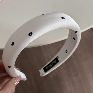 Detail of white padded satin headband with black daisy prints and inner woven label