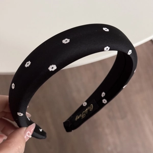 Detail of black floral satin scrunchie headband showing brand label and fabric texture